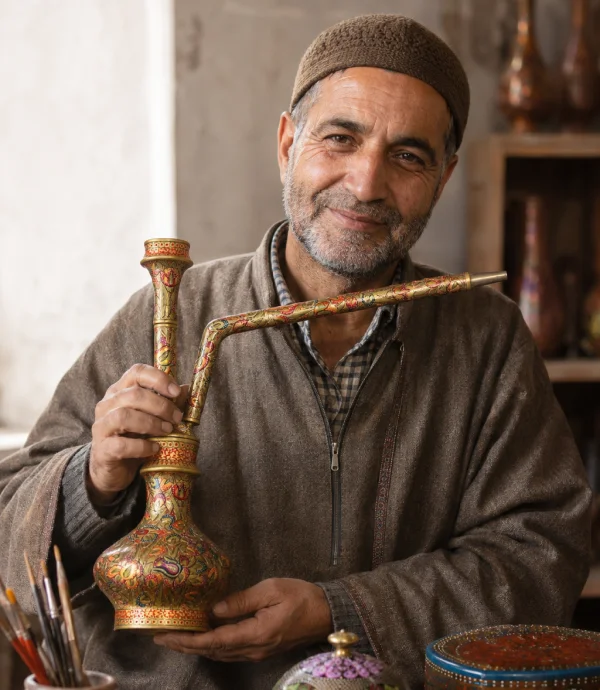 Kashmiri artisan holding a handcrafted decorative vessel while demonstrating traditional papier-mâché craftsmanship in a workshop setting.