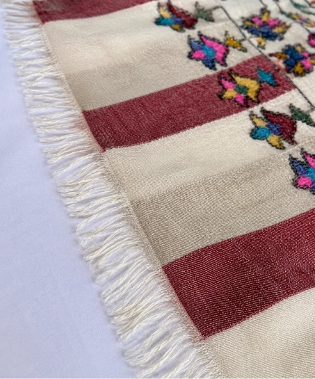 Close-up of the handcrafted Kashmiri shawl featuring decorative striped borders, colorful floral motifs, and neatly finished fringed edges.