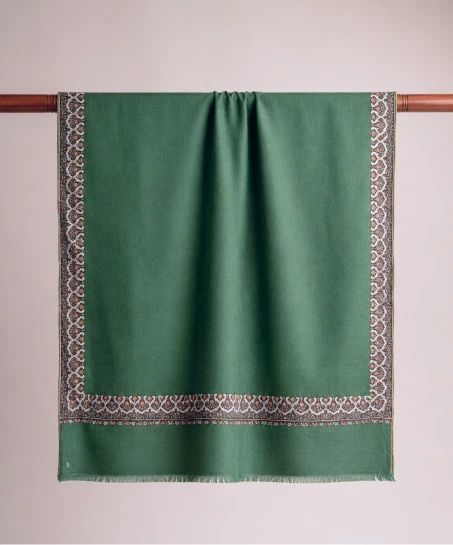 Handcrafted Kashmiri embroidered shawl displayed flat, featuring a solid emerald green body with finely embroidered floral borders and delicate fringed edges.