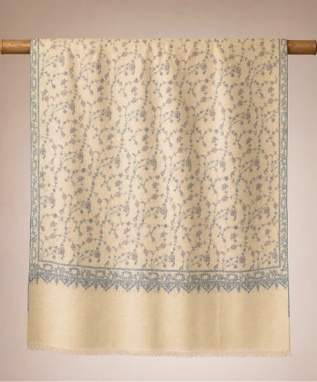 Handcrafted Kashmiri embroidered shawl displayed flat, featuring an ivory body with all-over floral vine embroidery, blue embroidered borders, and finely finished fringed edges.
