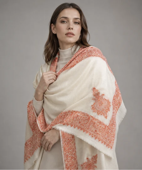 Model wearing a handcrafted Kashmiri embroidered shawl in ivory featuring intricate paisley embroidered borders, floral corner motifs, and a soft woven finish.