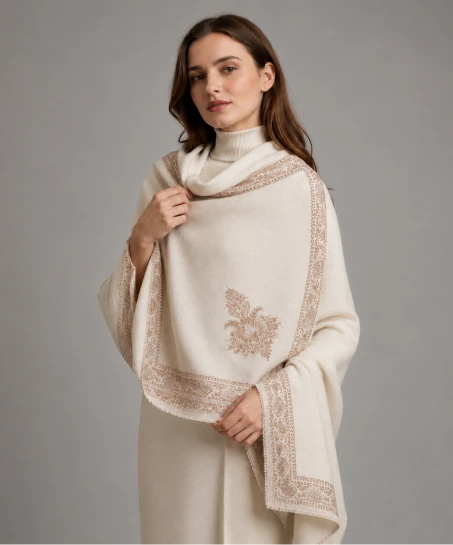 Model wearing a handcrafted Kashmiri embroidered shawl in ivory with intricate floral border embroidery and elegant corner motifs on a soft woven fabric.