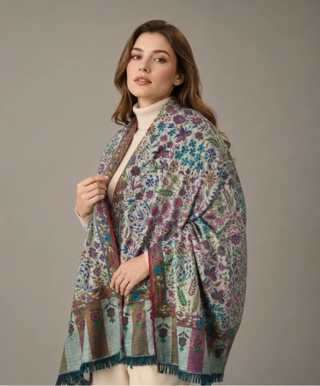 Model wearing a handcrafted Kashmiri woven shawl featuring all-over floral motifs, multicolor woven detailing, decorative striped borders, and soft tasseled fringes.
