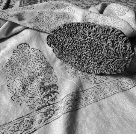 Traditional hand-carved wooden printing block placed on fine fabric with intricate floral patterns, highlighting the craftsmanship used in Kashmiri textile printing.